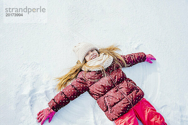 Carefree girl lying down on snow in winter