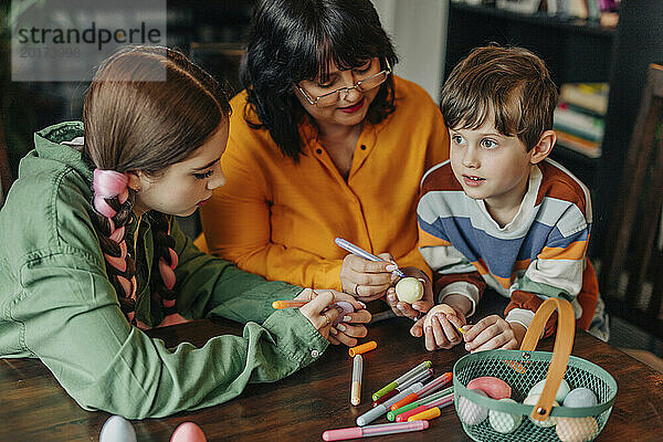 Glückliche Großmutter mit Enkelkindern  die Ostereier bemalen