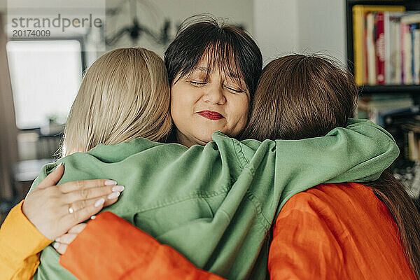 Lächelnde Mutter umarmt ihre Töchter zu Hause