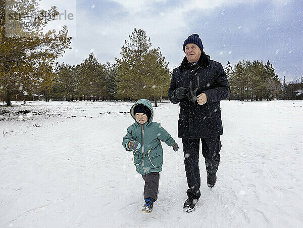 Älterer Mann geht mit Enkel auf Schneefeld