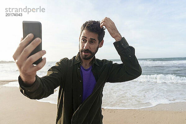 Mann macht an einem sonnigen Tag ein Selfie per Smartphone am Strand
