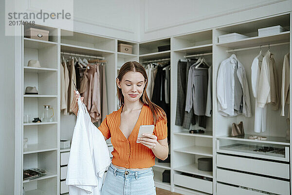 Lächelnde Frau benutzt Smartphone in der Nähe von Schrank