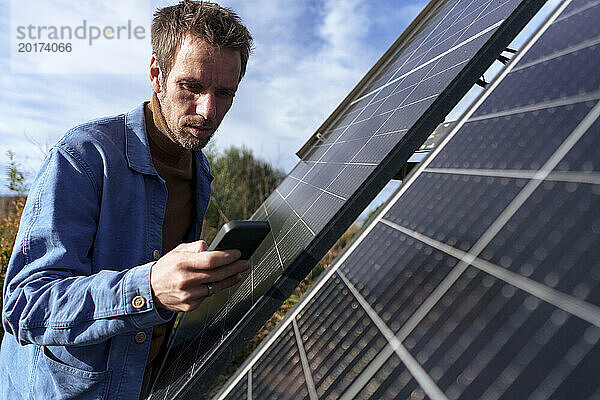 Mann benutzt Smartphone an sonnigem Tag in der Nähe von Solarpanel