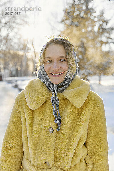 Lächelnde junge Frau mit Kopftuch und Pelzmantel im Winter