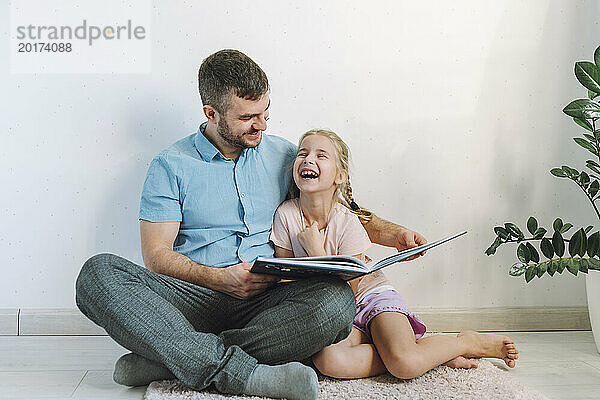 Glücklicher Mann liest seiner Tochter zu Hause vor der Wand ein Buch vor