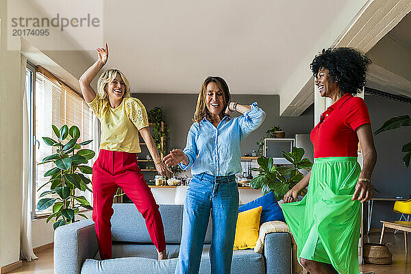 Fröhliche Freunde tanzen zu Hause neben dem Sofa im Wohnzimmer