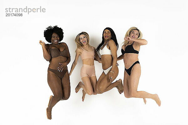 Cheerful women and non binary person jumping against white background
