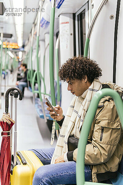 Mann mit Gepäck sitzt im Zug und benutzt Smartphone