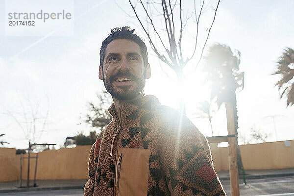 Happy man wearing sweater and standing under sky on sunny day