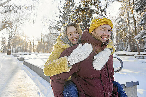 Glücklicher Mann gibt einer Frau Huckepackfahrt im Schnee im Winterwald