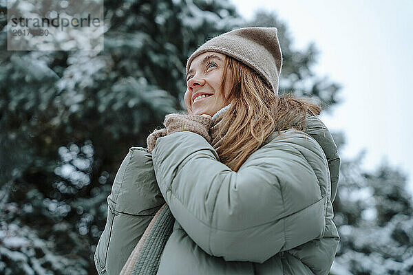 Lächelnde Frau in warmer Kleidung und Tagträumen im Winter