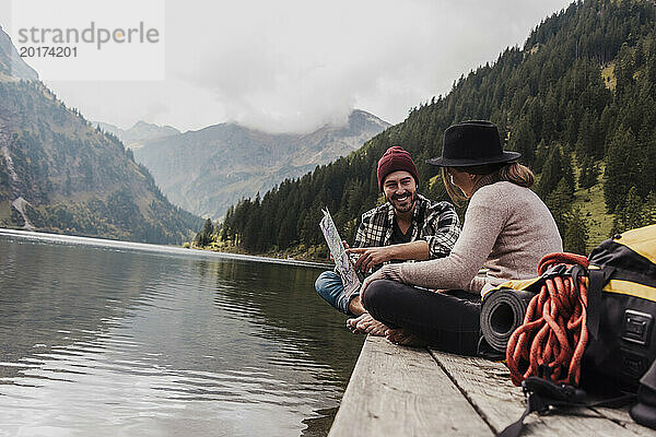 Happy young couple sitting with map on pier near lake Vilsalpsee and mountains at Tyrol  Austria