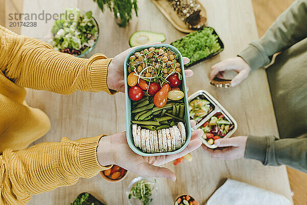 Hände einer Frau halten eine Lunchbox mit vegetarischem Essen neben einem Mann am Tisch