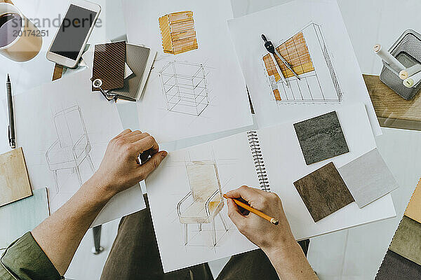 Möbeldesigner skizziert Stuhldesign auf Buch am Schreibtisch im Büro