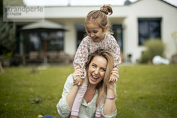 Glückliche Mutter mit Tochter  die auf Schultern in der Nähe des Hauses sitzt