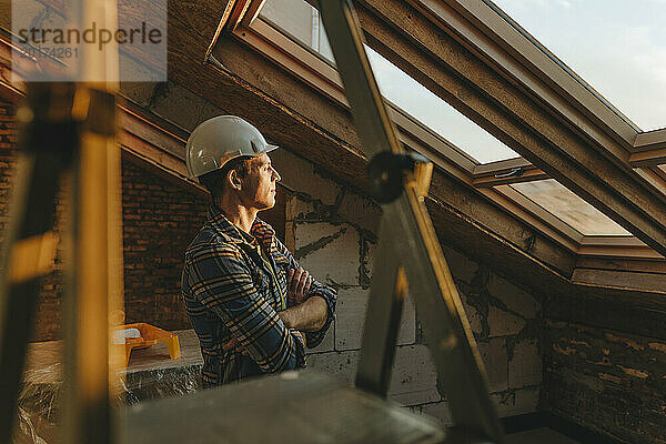 Architekt trägt Schutzhelm und blickt aus dem Fenster auf die Baustelle