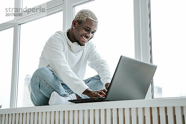 Lächelnder Freiberufler mit Laptop am Fenster zu Hause