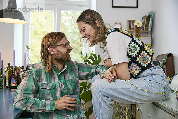 Glücklicher Mann hält Kaffeetasse in der Hand und sitzt mit Frau zu Hause