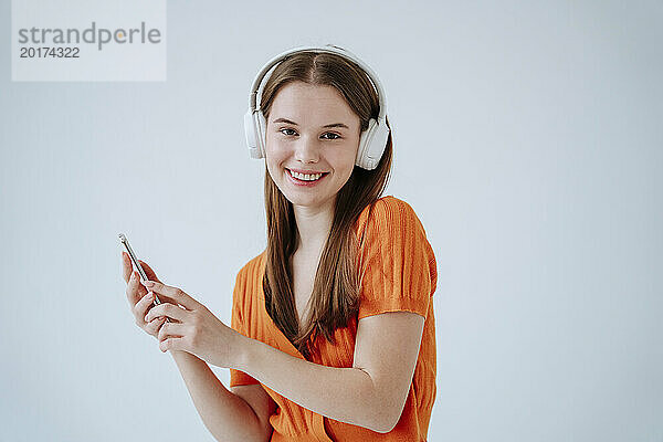 Lächelnde Frau  die vor weißem Hintergrund Musik über kabellose Kopfhörer hört