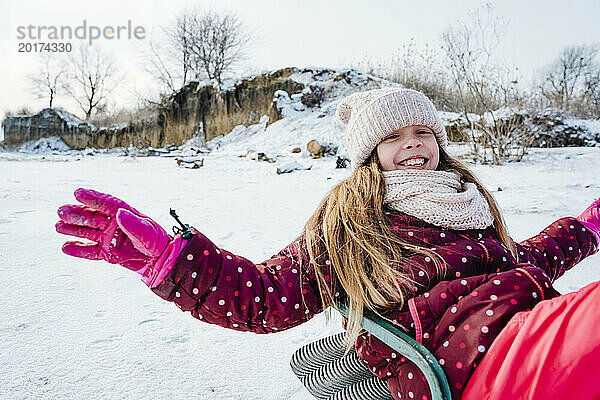 Fröhliches Mädchen  das im Winter eine Schlittenfahrt im Schnee genießt
