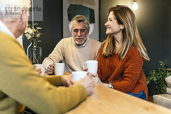 Glückliche Freunde mit Kaffeetasse  die am Tisch diskutieren
