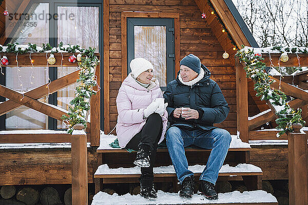 Älteres Paar sitzt und trinkt Tee auf der Veranda in der Nähe der Blockhütte