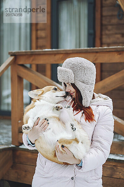Junge Frau hält Corgi-Hund vor Blockhütte