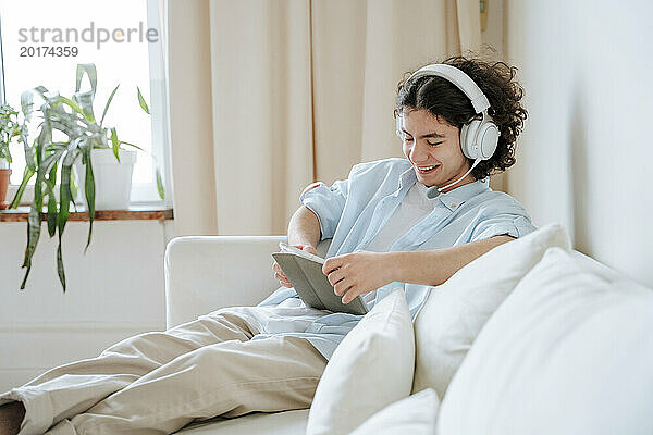 Lächelnder Mann mit Headset und Tablet-PC auf dem heimischen Sofa