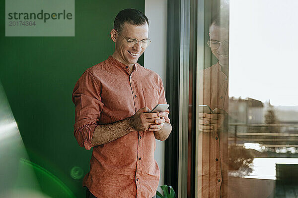 Glücklicher Mann benutzt Smartphone in der Nähe einer Glastür
