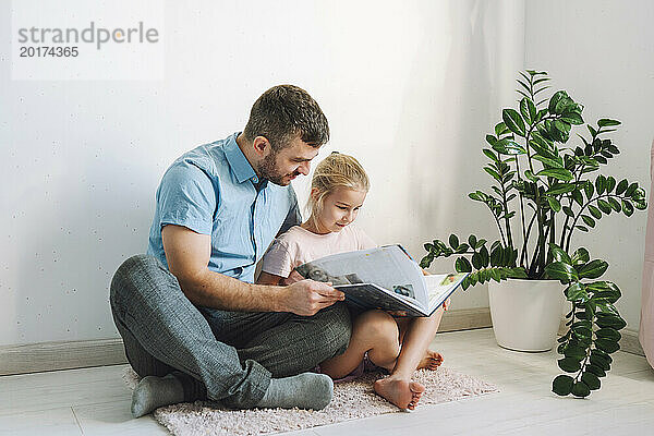 Vater und Tochter sitzen auf dem Boden und lesen zu Hause ein Buch