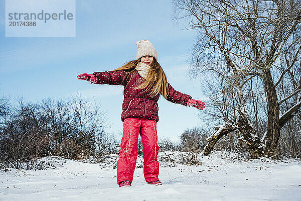 Glückliches Mädchen  das im Winter mit ausgestreckten Armen auf dem Schnee steht