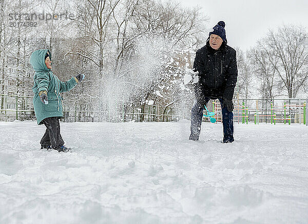 Glücklicher Junge spielt mit Großvater im Schnee im Park