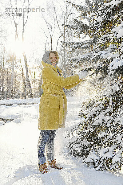 Glückliche junge Frau steht im Winter und berührt den Tannenbaum