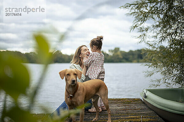 Glückliche Frau  die Spaß mit Tochter in der Nähe von Hund am See hat