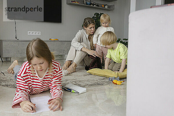 Kinder spielen mit Mutter und Mädchen und machen zu Hause Hausaufgaben