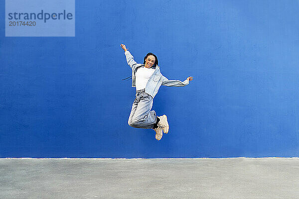 Fröhliche Frau springt vor blaue Wand