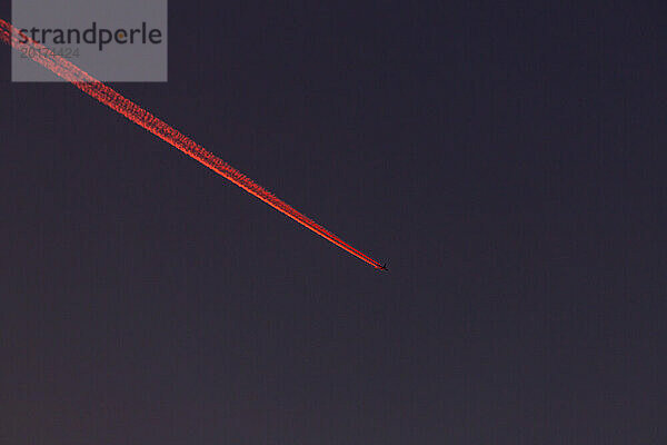 Flugzeug hinterlässt nachts rote Kondensstreifen am Himmel