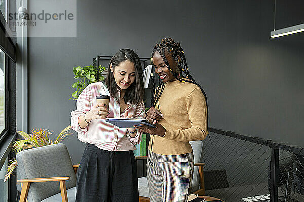 Geschäftsfrau hält Kaffeetasse in der Hand und diskutiert mit Kollege über Tablet-PC