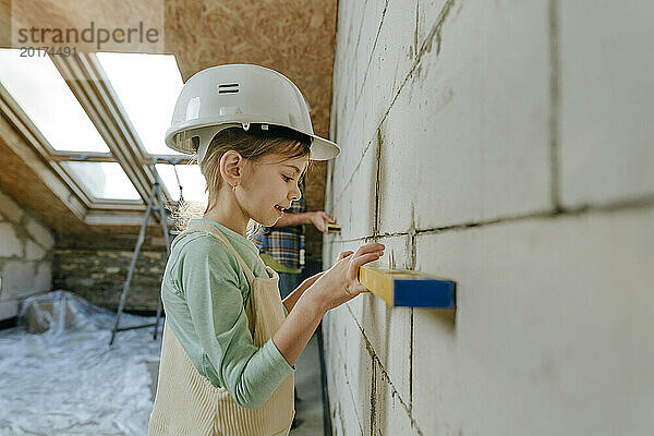Mädchen benutzt Nivelliergerät an der Wand in einem Zimmer  das gerade renoviert wird