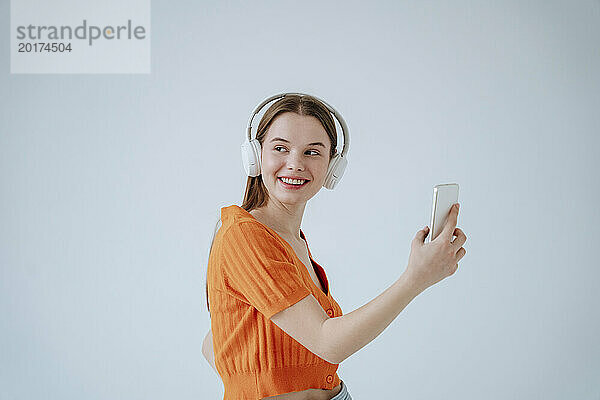 Lächelnde Frau trägt kabellose Kopfhörer und hört Musik vor weißem Hintergrund