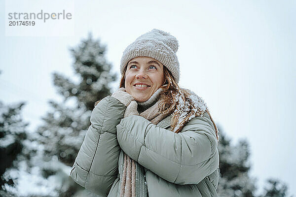 Lächelnde Frau in Jacke und Tagträumen im Winter