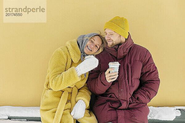 Glückliches Paar genießt gemeinsam Kaffee vor gelber Wand