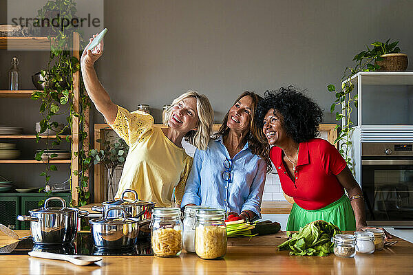 Lächelnde Freunde machen zu Hause in der Küche ein Selfie mit dem Smartphone