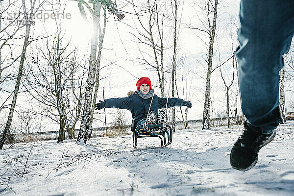 Fröhlicher Sohn genießt im Winter eine Schlittenfahrt im Schnee
