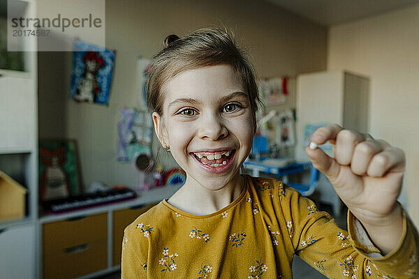 Happy girl holding broken tooth at home