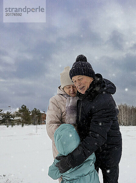 Glückliches älteres Paar umarmt Enkel auf Schneefeld