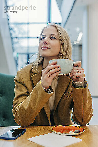 Nachdenkliche Frau trägt braune Jacke und trinkt Kaffee im Café