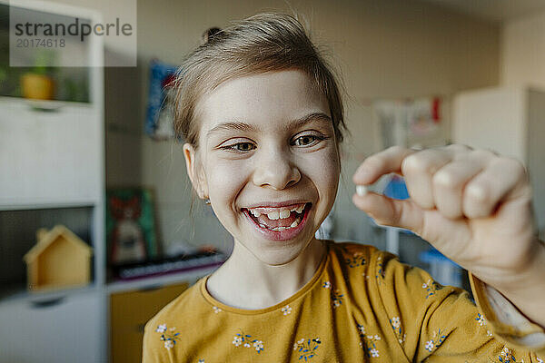 Cheerful girl holding broken tooth at home