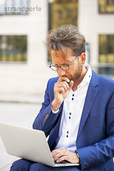 Nachdenklicher Geschäftsmann  der in der Stadt am Laptop arbeitet