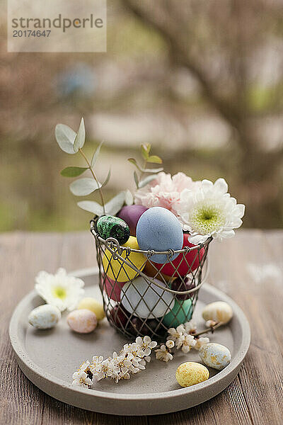 Bunte Ostereier mit Blumendekoration im Korb auf Tablett